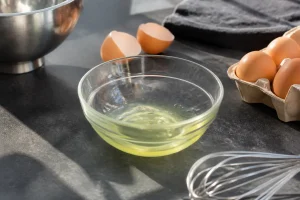 Bol contenant du poids blanc d'œuf près de coquilles et fouet de cuisine