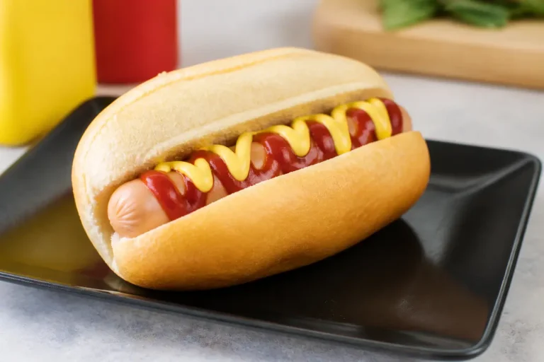 Hot dog avec moutarde et ketchup sur assiette noire, idéal pour recette de hot dog